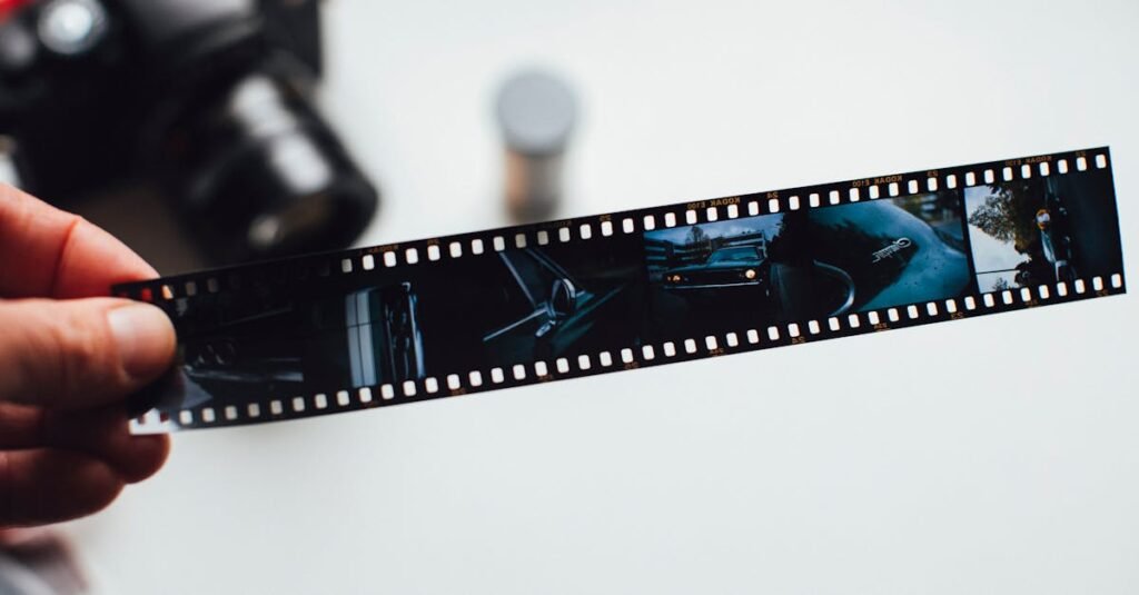 Close-up of a hand holding a vintage film strip with a blurred camera in the background, evoking nostalgia.