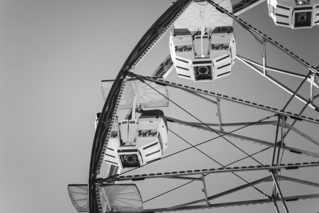 Black and white photo of a Ferris wheel at a funfair, capturing geometry and design in an amusement park setting.